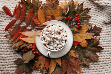 Autumn morning coffee. Cup of coffee with marshmallow and cinnamon on a plaid against the background of autumn leaves. Still life concept.
