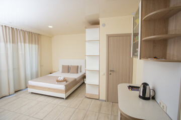 The bedroom has a large bed with white sheets and pillows in the hallway there is a kettle on the table