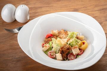 Classic Caesar Salad with grilled chicken, croutons, cherry tomatoes in a white plate on a wooden table with a fork