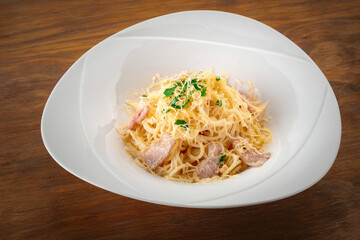Spaghetti pasta with bacon, cheese and herbs on a white plate on a wooden background