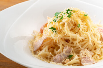 Spaghetti pasta with bacon, cheese and herbs on a white plate on a wooden background, close up