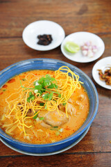 Traditional Northern Thai food (Khao Soi), spicy curry noodles soup with coconut milk and chicken in a bowl on wooden background, Asian food, Top view