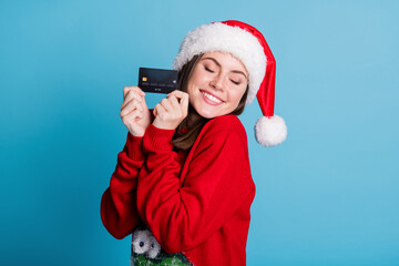 Photo portrait of glad woman holding credit card in two fingers hands eyes closed isolated on pastel light blue colored background