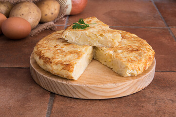 Spanish omelette made with potatoes, eggs and onion, with a piece of parsley on top, on a wood board in a rustic kitchen with a piece of parsley on top