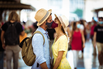 Tourist with face mask kissing in the city - New normal lifestyle concept with couple in love kiss outdoor - Tourism, love and corona virus.