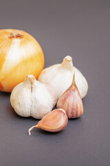 Unpeeled raw bulb and clove of garlic and onion on black surface with empty space for text