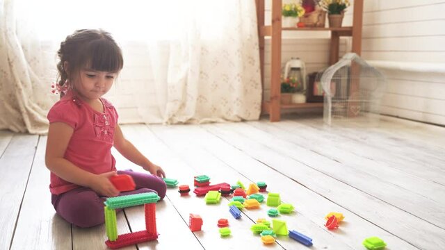 Little beautiful girl sits on the floor in the room and plays with a colorful constructor