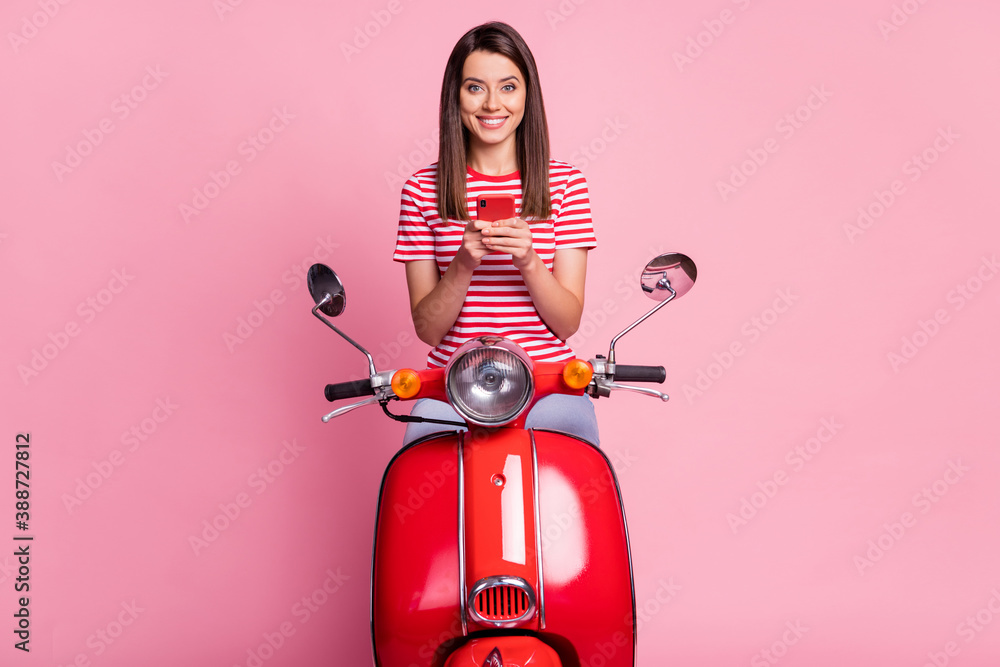 Sticker Photo portrait of pretty woman sitting on red moped keeping mobile phone smiling isolated on pastel pink color background