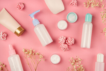 Obraz na płótnie Canvas Soap and cream bottles with small flowers on pink background. Packaging of cream, lotion, gel, facial foam or skin care. Cosmetic beauty product branding mock-up