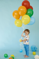 Fototapeta na wymiar Full length portrait of cheerful boy holding balons posing against blue background