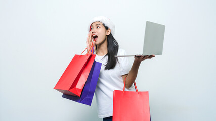 Beautiful attractive Asian woman with santa hat holding shopping bag and laptop in studio shot.