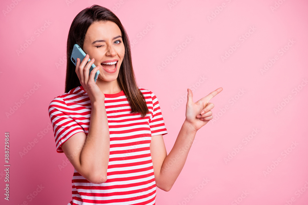 Sticker Photo portrait of girl talking on cell phone pointing finger at blank space winking isolated on pastel pink color background