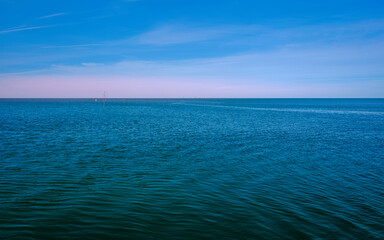 Tranquil seascape with gentle blue waves and soft white clouds on the blue sky background at dusk