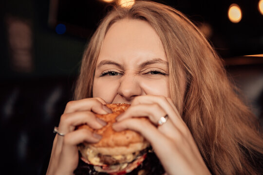 Portrait of a young lovely hungry woman sitting in the street fast junk food restaurant cafe with open mouth bite and eating enjoying a fresh tasty burger. Image with copy space.