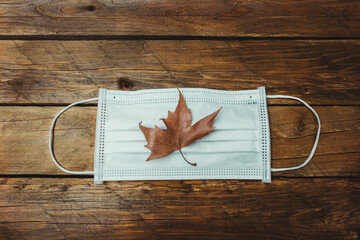 Mascarilla con hoja de oto&ntilde;o en un fondo de madera. coronavirus