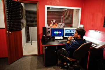 Young asian singer with microphone recording song in record music studio with sound producer.