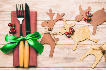 Top view of new year utensils on napkin with holiday decorations and reindeer on wooden background. Close up of christmas dinner concept