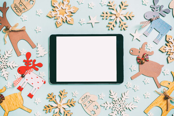 Top view of digital tablet on blue background made of holiday decorations and toys. Christmas ornament concept