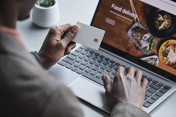 Close-up of man sitting at the table in front of laptop with credit card ordering food online