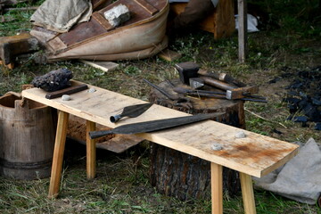 A close up on two metal weapon elements laying on a wooden bench next to some blacksmith equipment...