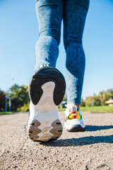 White sneakers with black inserts on female legs dressed in jeans on an asphalt road