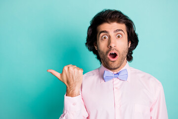 Photo of surprised gentle man wear pink shirt pointing one thumb finger look empty space isolated turquoise color background