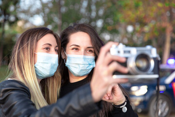 Close up of two girls wearing face masks with an analog camera in their hands.