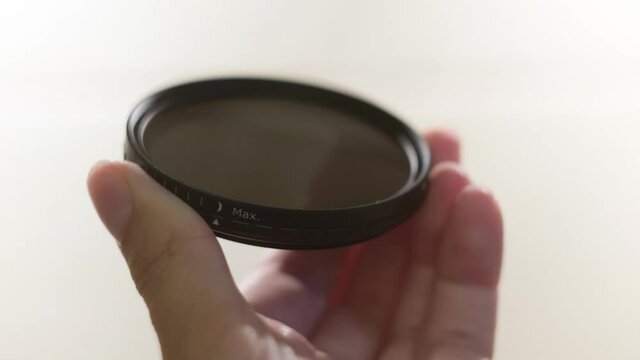 Close up of polarizing lens filter in girls hands isolated on white background. Concept. Woman turning into the both sides mechanism of lens filter.