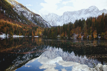 Autumn landscape of mountains covered in snow and reflected in blue italian lake.