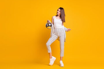 Full size photo of cheerful nice brown hair girl hold disco ball look wear suit tank-top sneakers isolated over yellow background