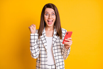 Photo portrait of surprised shocked businesswoman gesturing like winner shouting keeping phone isolated on vivid yellow color background