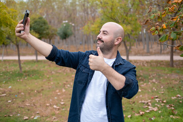 Naklejka na ściany i meble Bald charismatic man making video call with phone in the park in autumn. bald and mustache charismatic model