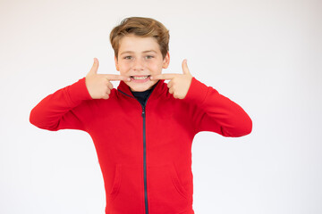 Portrait of teen boy showing his teeth. Child pointing with finger teeth and mouth. Caucasian young teenager, isolated on white background. Concept of good teeth care. Dental health concept.