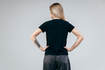 Back of stylish blonde girl wearing black t-shirt posing in studio
