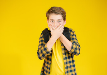 Cute little boy is covering his mouth and looking at camera, on yellow background