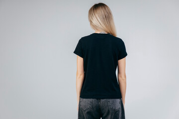 Back of stylish blonde girl wearing black t-shirt posing in studio
