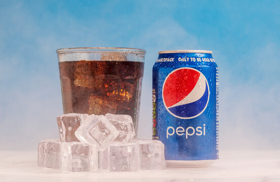 London, United Kingdom - October 29 2020:  Ice cold can or Pepsi sits next to a full glass of soda with condensation and ice cubes.  Fog from the cold forms over the marble surface and blue wall.