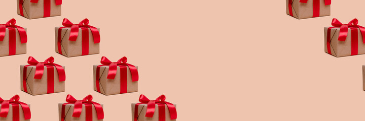 Pattern made of gift boxes tied with red ribbons on a beige background with copy space. Festive banner.