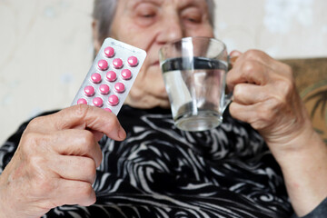 Elderly woman with pills in and glass of water. Concept of medical prescription, sedatives, heart or sleeping pill