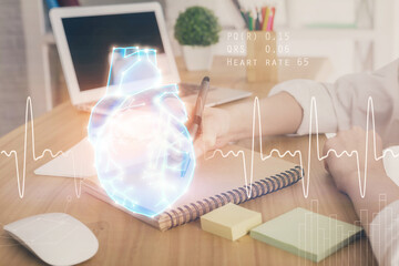 Heart hologram over woman's hands writing background. Concept of Medical study. Multi exposure