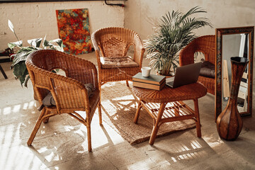 Luxurious and comfortable hotel room in daytime with bamboo chairs and table there are laptop and books with plant on it.