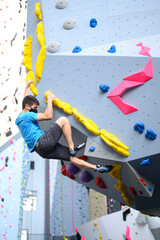 man wearing a COVID-19 pandemic mask climbs a bouldering wall in a climbing gym following social...