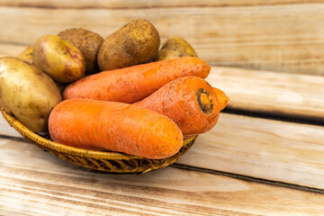 Carrots, potatoes in a wicker plate on a wooden background.