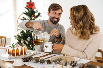 Obraz na płótnie Canvas Happy couple drinking tea with pie while having Christmas dinner