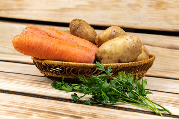 Carrots, potatoes and greens in a wicker plate on a wooden