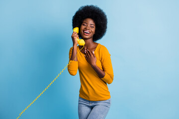 Photo portrait of black skinned woman talking on retro telephone keeping handset with wire laughing isolated on bright blue color background