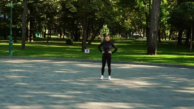 Sporty woman in black training costume warming up feet in park and starting running, yellow leaves lying on ground. Arc shot jogger training outside in early autumn. Concept of fitness