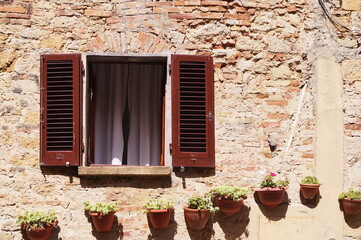 Fototapeta na wymiar Window of a house in Volterra with flower pots attached to the wall, Tuscany, Italy