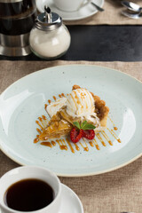 Slice of apple pie with a scoop of ice cream on top with raspberry and cup of coffee at restaurant