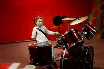 child in a mask plays drums on a red background, a child plays a drum kit, the concept of musical...